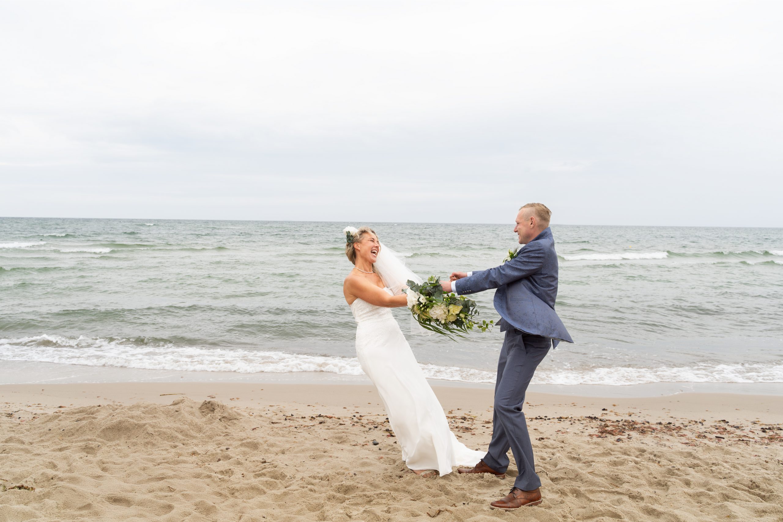 Brautpaar hält Hände im Wind am Strand, Hochzeit an der Ostsee